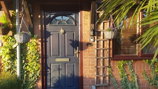 A brick house with a dark wooden door, a small garden with gravel and plants, and a metal fence. - Cyrus House Thameside (London)
