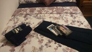 A bed with floral bedding, a brown headboard, and a wooden nightstand with a lamp. - Cyrus House Thameside (London)