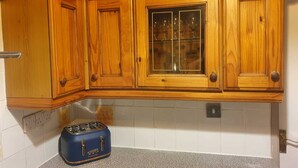 A kitchen with wooden cabinets, a glass-fronted cabinet, and a blue toaster on the countertop. - Cyrus House Thameside (London)