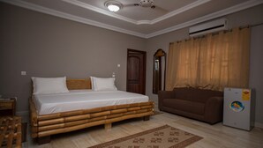 A bedroom with a bed, a brown sofa, a ceiling fan, an air conditioner, and a patterned rug. - Aborigines beach resort (Keta)