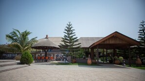 A covered outdoor area with a tiled floor, a thatched-roof structure, and a building with a corrugated metal roof. - Aborigines beach resort (Keta)