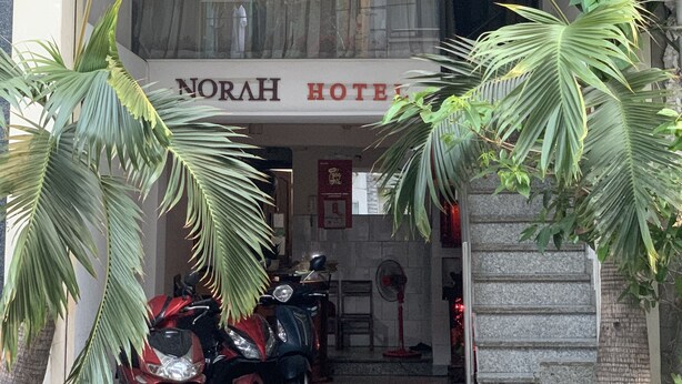 La entrada del Hotel Vientiane, con un letrero que muestra el nombre y la dirección del hotel, un amplio ventanal y una motocicleta estacionada afuera.