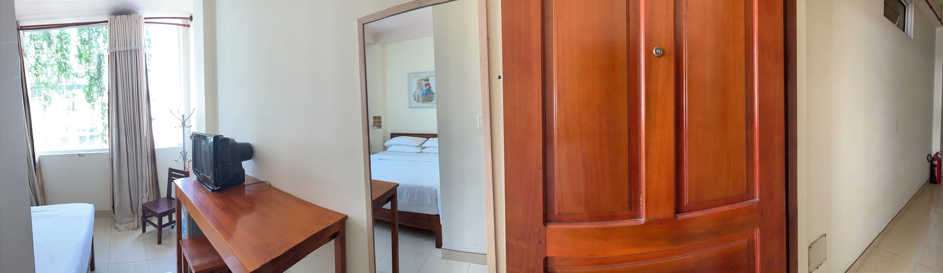 Une chambre d’hôtel avec un bureau en bois, un lit, une fenêtre avec des rideaux et une porte.