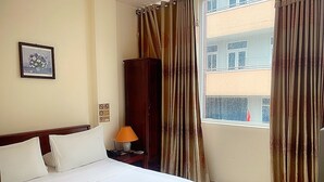 Habitación de hotel con cama, mesita de noche con lámpara, armario y ventana con cortinas.