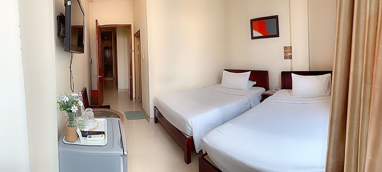 A hotel room with two beds, a desk with a computer, a TV, and a small table with a vase of flowers.