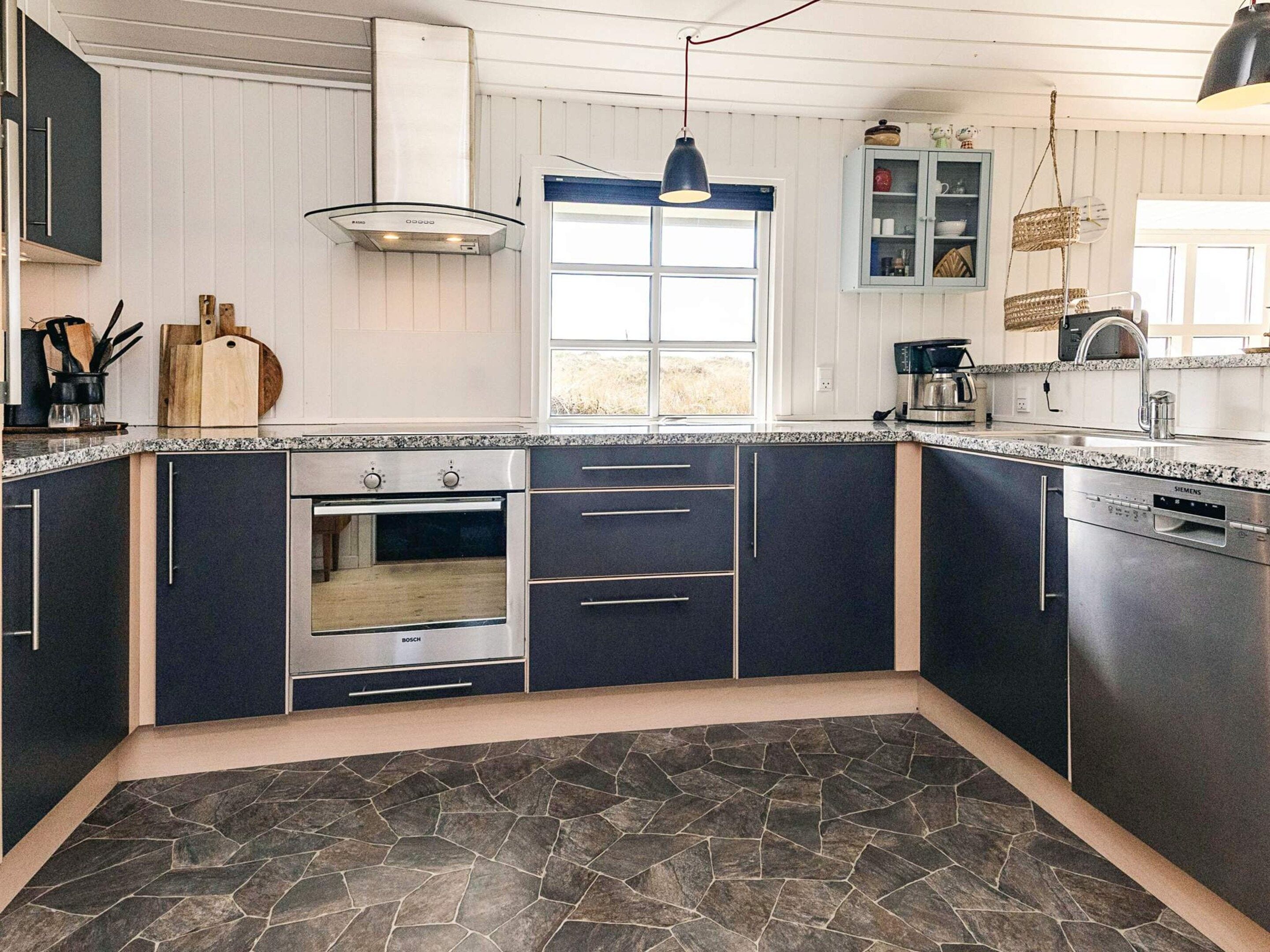 A modern kitchen with dark cabinetry, a Bosch oven, a Siemens dishwasher, and a stone-patterned floor.