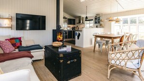 A cozy living room with a fireplace, a dining area, and a kitchen. - 4 Star Holiday Home in Lokken (Lokken)