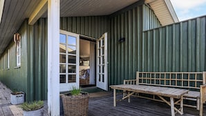 A wooden deck with a bench and potted plants, a building entrance with a door, and a corrugated metal wall. - 4 Star Holiday Home in Lokken (Lokken)