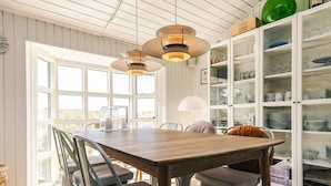 A dining area with a wooden table and metal chairs, a glass cabinet with dishes, and a large window with a view. - 4 Star Holiday Home in Lokken (Lokken)