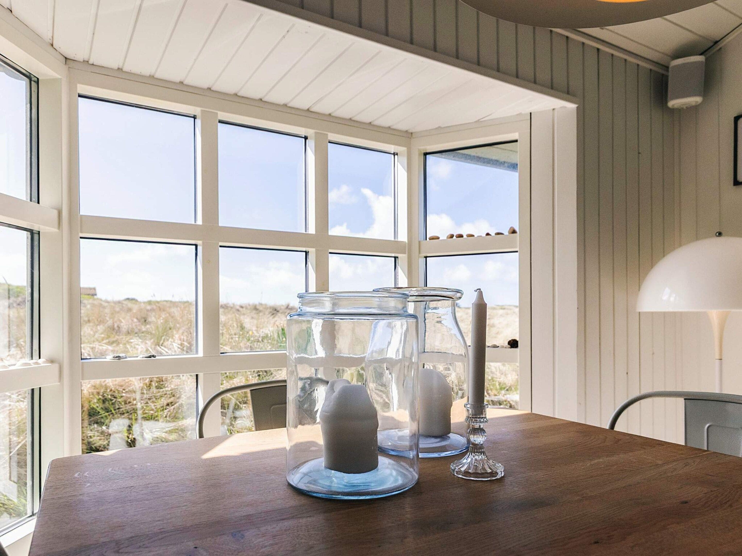 A room with a wooden table, clear glass candle holders, and a white lamp.