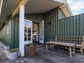 A wooden deck with a bench and a wicker basket, a building entrance with a door, and a corrugated metal wall. - 4 Star Holiday Home in Lokken (Lokken)