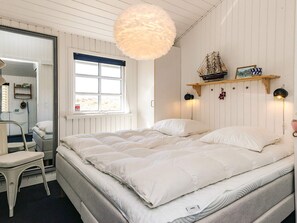 A bedroom with a bed, a chair, a window, and a wall-mounted shelf with decorative items. - 4 Star Holiday Home in Lokken (Lokken)