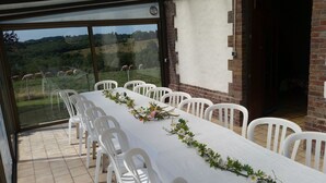 A dining area with a long table set for six, white chairs, and a view of grazing cows through large glass windows. - vacation home   (Hugleville-en-Caux)