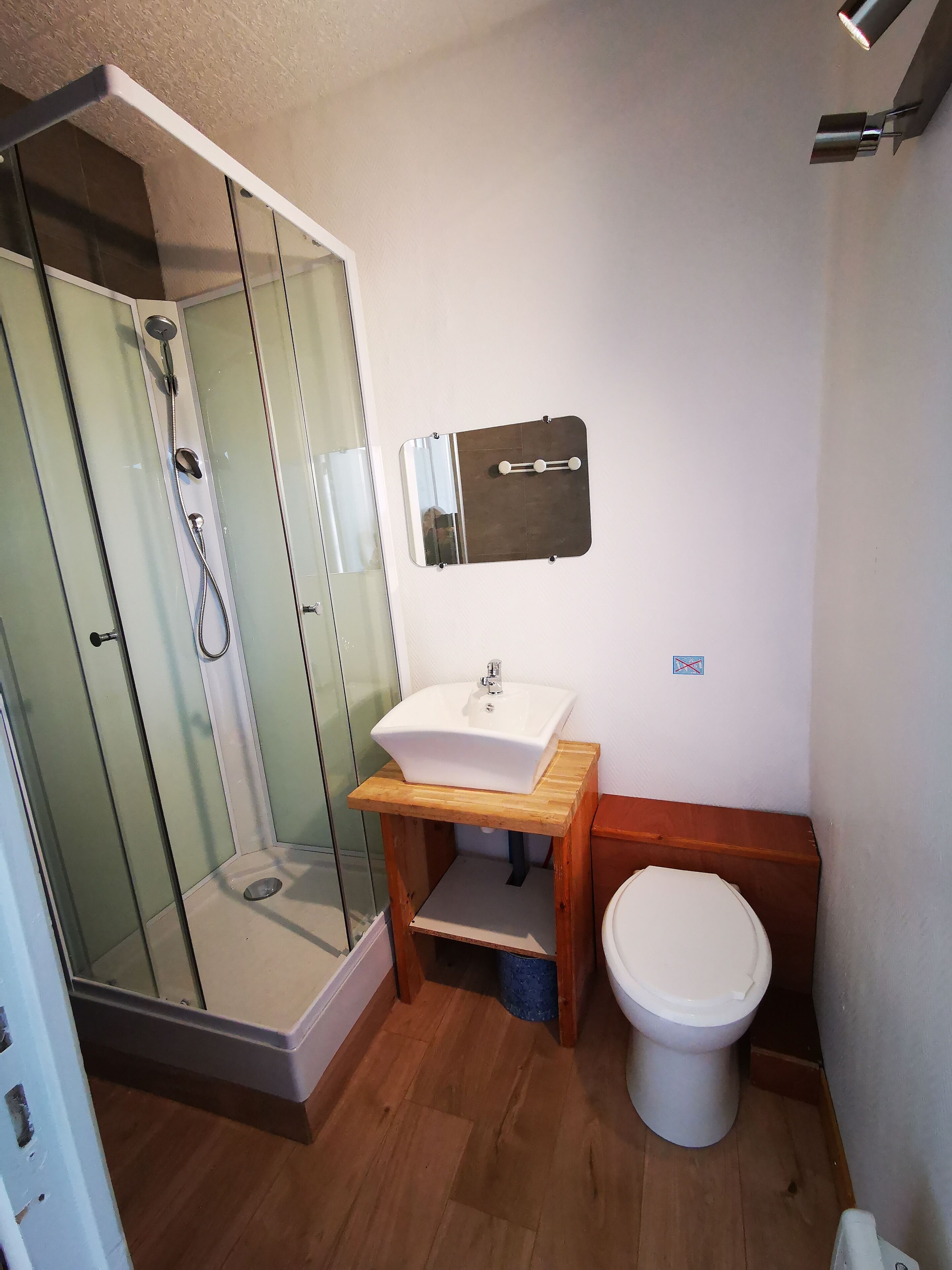 A bathroom with a glass shower enclosure, a white sink with a wooden countertop, and a white toilet.
