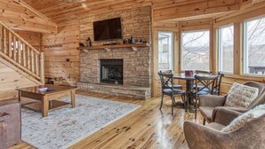 A wooden interior with a fireplace, a television mounted above it, and a dining area with chairs and a table. - ⭐️Prime Location with Stunning Views, Hot Tub, Game Room⭐️ (Gatlinburg)