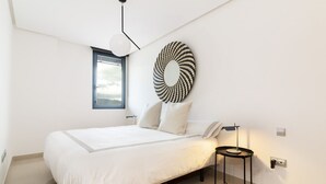 A modern bedroom with a bed, a bedside table, a wall-mounted lamp, and a window.