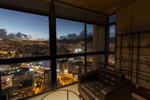A high-rise room with large windows offering a cityscape view at dusk.