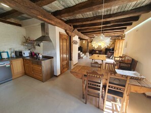 Una cocina rústica con armarios de madera, microondas y estufa. Hay un comedor con mesa y sillas de madera.
