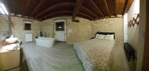Un dormitorio con una cama grande, una bañera integrada, una mesita de noche y un armario.