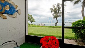 A room with a view of a lake, a boat, and a red flower arrangement. - Stunning Bay Views!  Come visit Paradise today! Call today for availability! (Bradenton Beach)