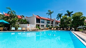 A swimming pool with lounge chairs and umbrellas, surrounded by palm trees and buildings with red roofs. - Stunning Bay Views!  Come visit Paradise today! Call today for availability! (Bradenton Beach)