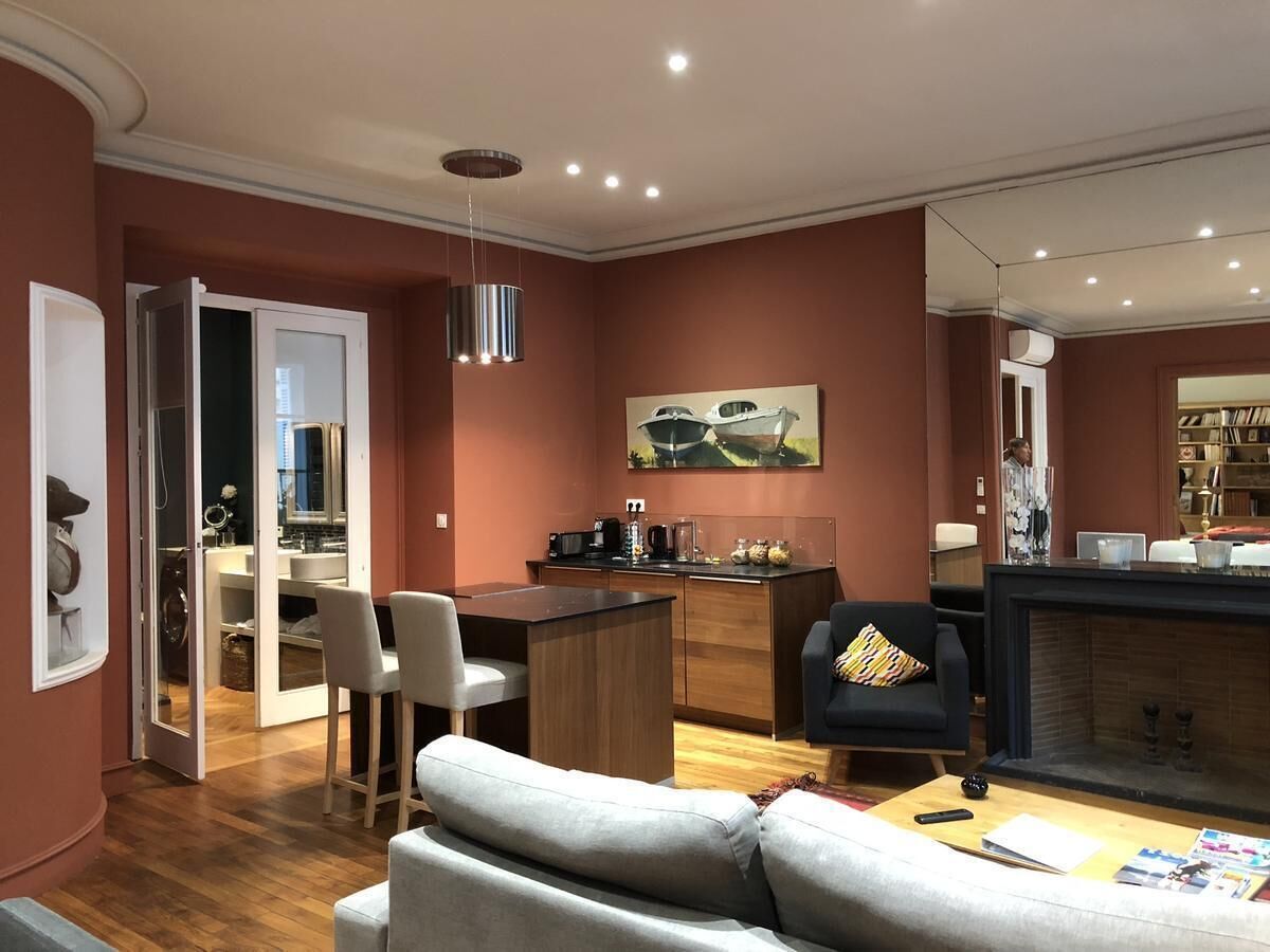 A modern living room with a sofa, a dining area with chairs, a kitchen with a counter, and a fireplace.