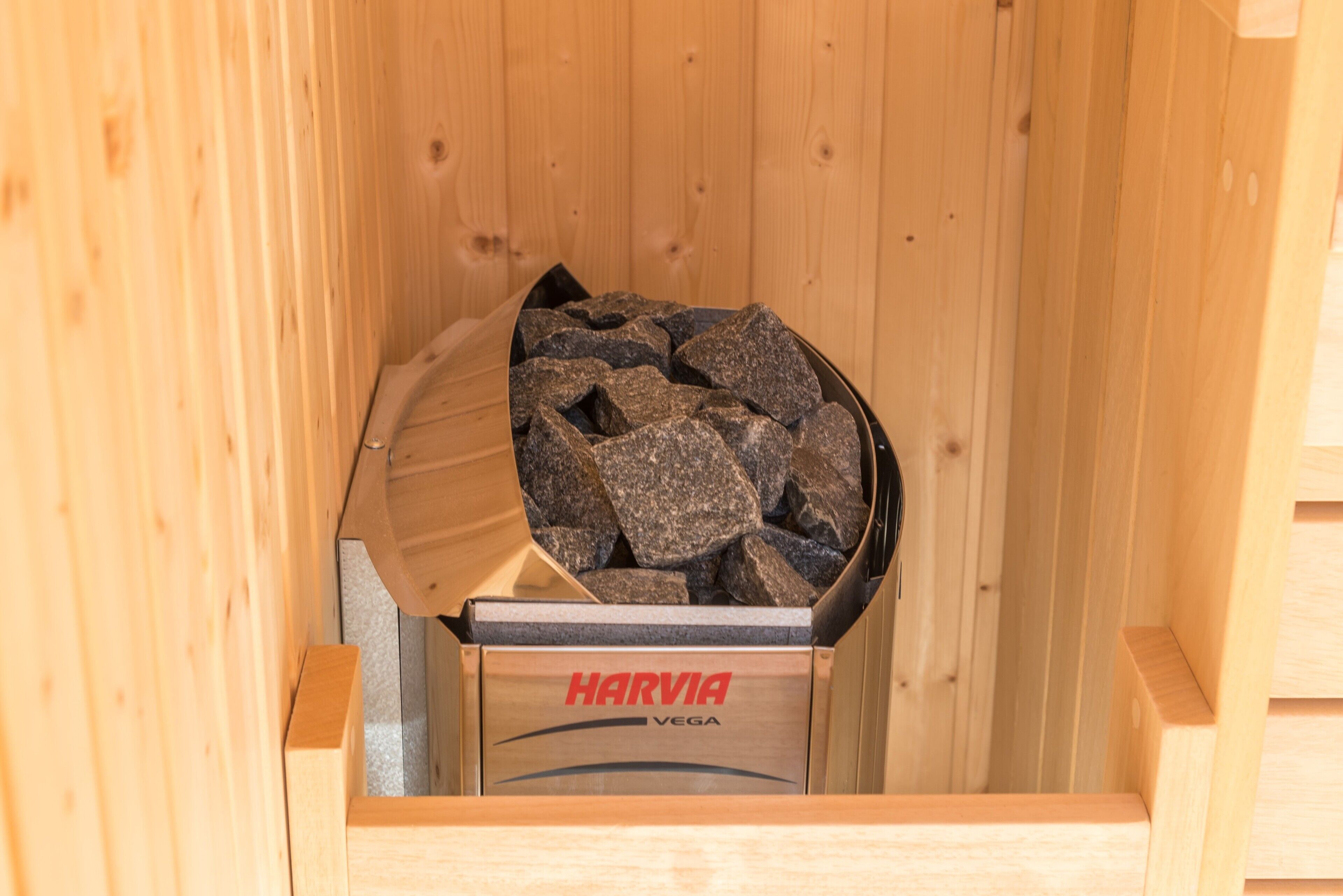 A wooden sauna with a Harvia Vega branded container filled with rocks.