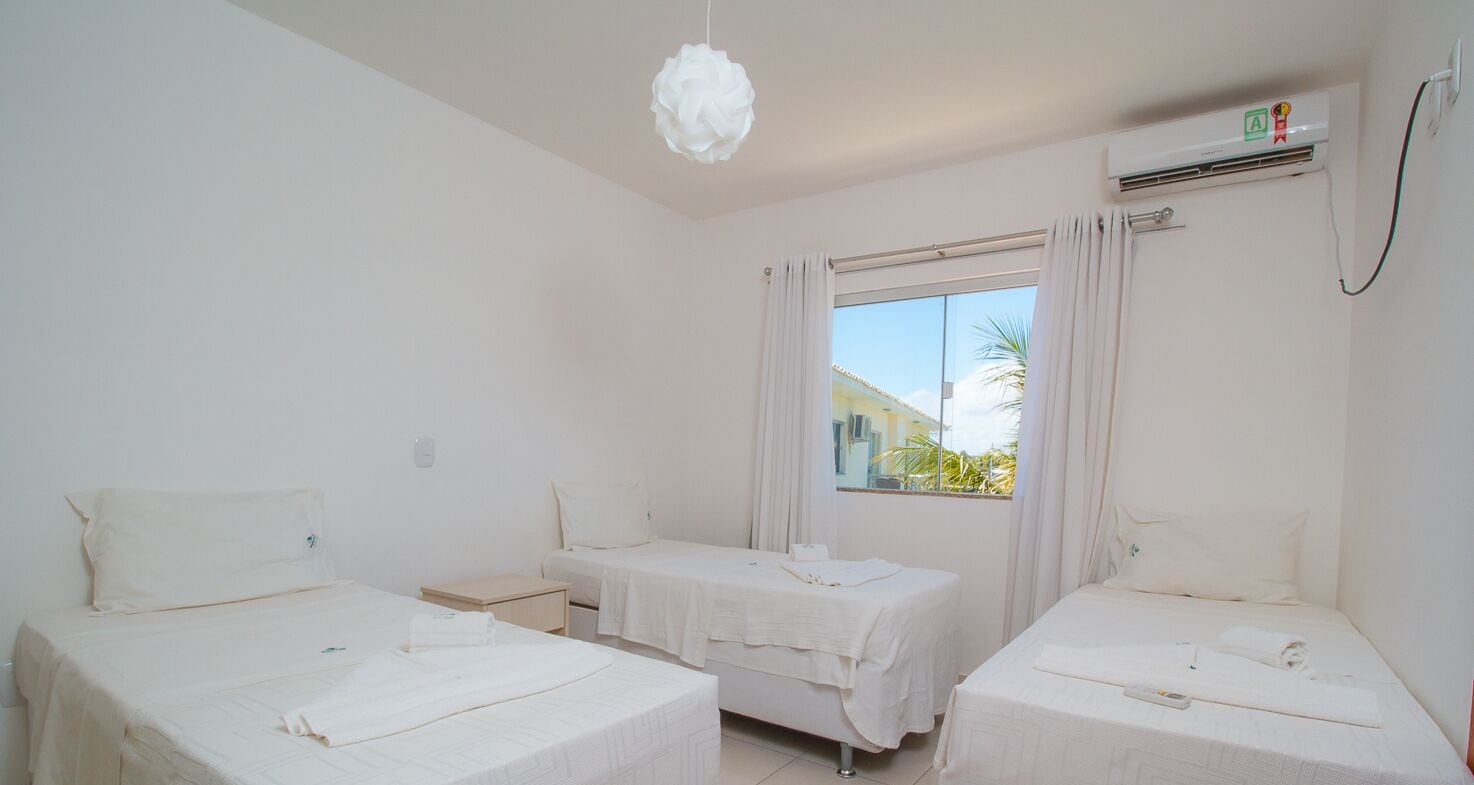 A hotel room with two single beds, a small bedside table, a window with curtains, and a ceiling light.