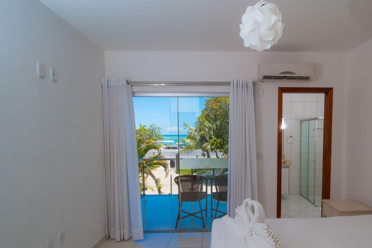 Habitación de hotel con balcón, cama, ducha y vista a la playa.