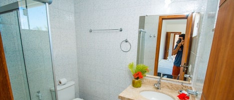A bathroom with a glass shower enclosure, a toilet, a sink with a marble countertop, and a mirror.