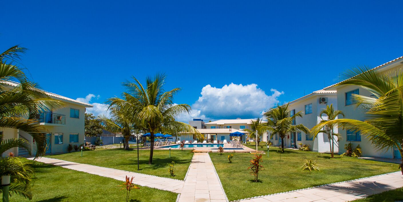 Een resort met meerdere gebouwen, een zwembad in het midden en palmbomen.