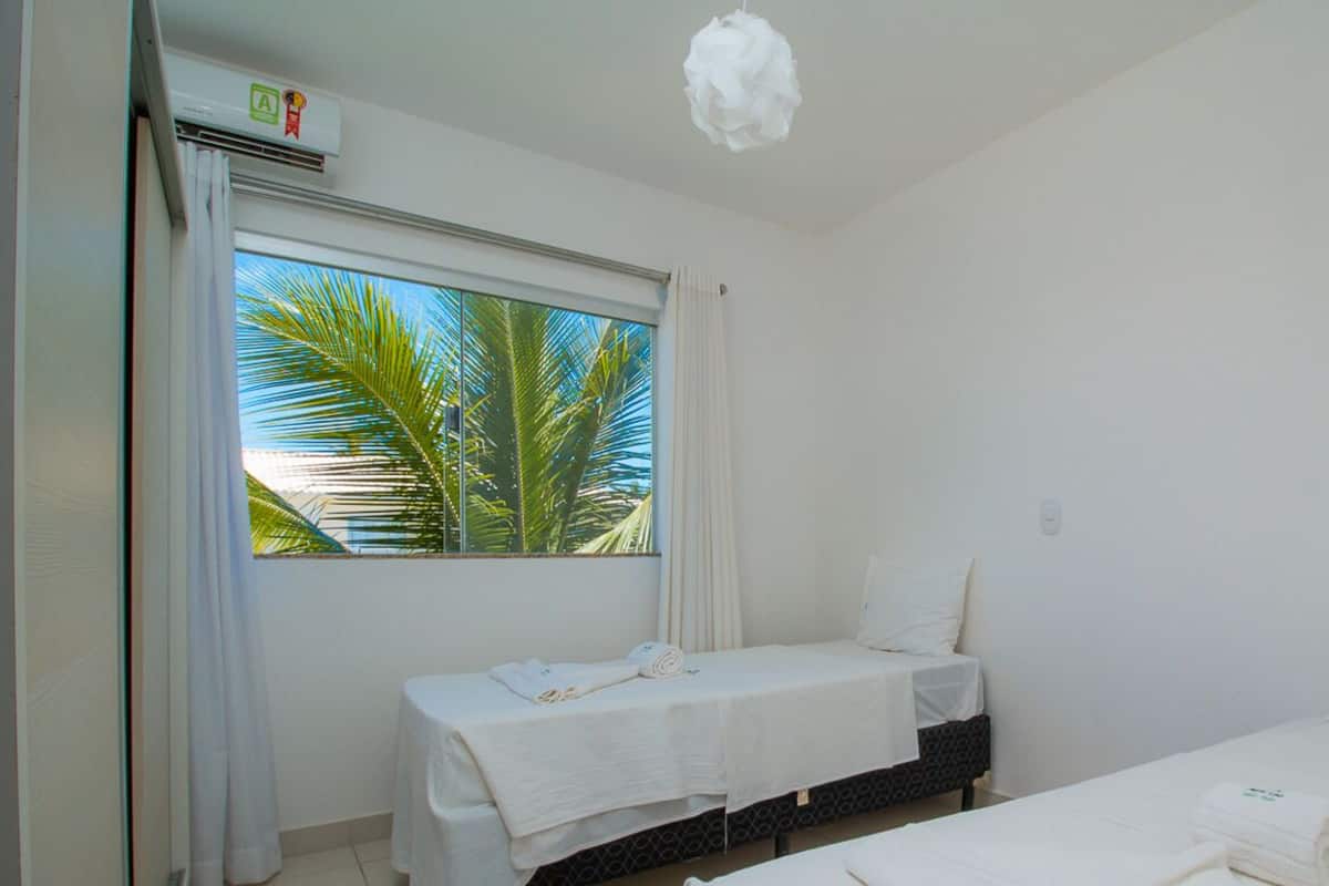 Una habitación de hotel con dos camas, una ventana que ofrece vistas a palmeras y una lámpara en el techo.