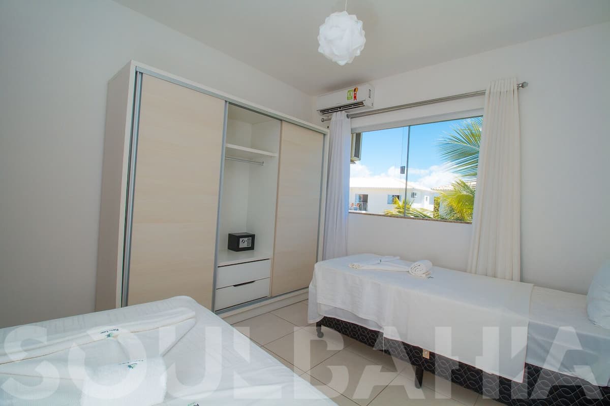 Un dormitorio con cama, armario, mesita y ventana con vista a palmeras.