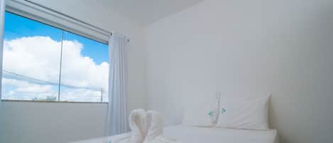 Habitación de hotel con cama, cortinas blancas y ventana que ofrece vista al cielo y nubes.