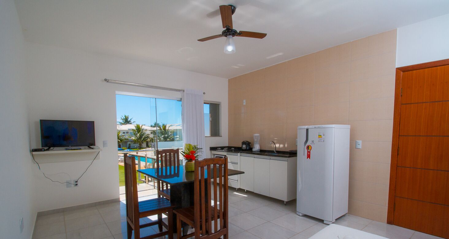 A compact kitchen with a dining area, a ceiling fan, a refrigerator, and a TV mounted on the wall.