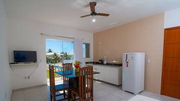 A compact kitchen with a dining area, a ceiling fan, a refrigerator, and a TV mounted on the wall.