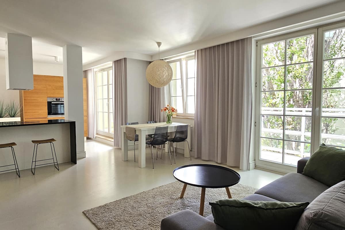 Una sala de estar moderna con un sofá, una mesa redonda de centro y un comedor con mesa y sillas.