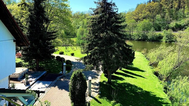 A view of a house with a paved driveway leading to a grassy area and a body of water.
