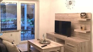 A modern living room with a TV, wooden furniture, a glass coffee table, and a view through a sliding glass door.