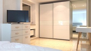 A modern bedroom with a bed, a TV, a wardrobe, and a bathroom visible through a glass door.