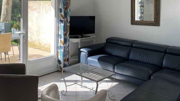A modern living room with a black leather sofa, a white chair, a TV on a white stand, and a ceiling lamp. - GITE 10 PERSONNES (Arles)