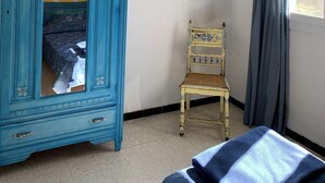 A room with a blue wardrobe, a small chair, a bed, and a window with curtains. - GITE 10 PERSONNES (Arles)