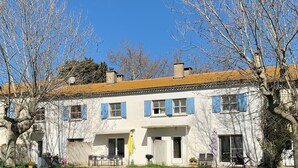 A two-story building with a white facade and blue shutters, a grassy yard, and trees. - GITE 10 PERSONNES (Arles)