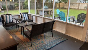 En overdækket terrasse med fletningsmøbler, et mønstret tæppe og udsigt til baghaven.