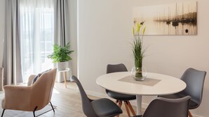 A modern dining area with a round table, grey chairs, and a vase with plants. - Apartments (Tivat)