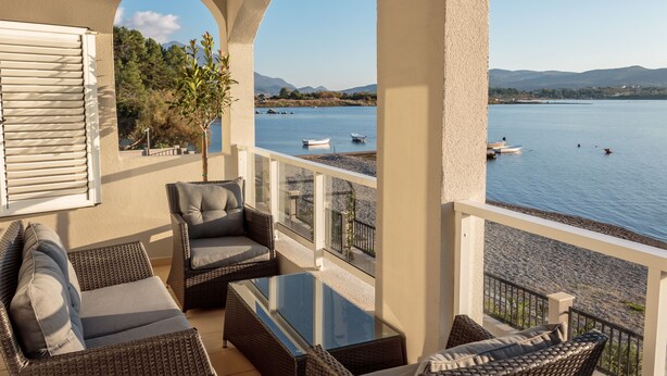 A balcony with wicker furniture, a glass table, and a view of a lake with boats. - Apartments (Tivat)