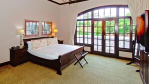 A bedroom with a large bed, two bedside tables with lamps, a dresser, and a large window with a view of greenery. - Audacia Manor Boutique Hotel (Berea)