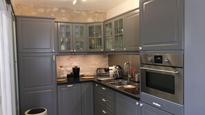 A compact kitchen with grey cabinets, a built-in oven, and a coffee machine. - Les Colonnes de Chanteloup (Amboise)