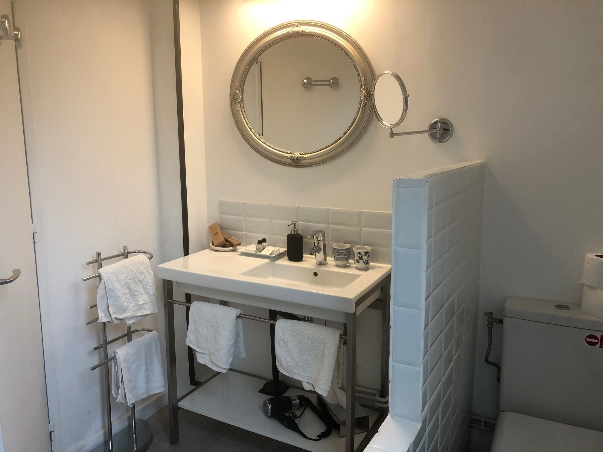 Ein Badezimmer mit weißem Waschbecken, einem Spiegel, einem Handtuchhalter und einer Toilette.