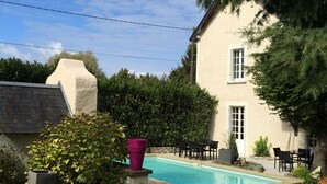 A pool area with a house in the background, surrounded by greenery and a clear sky. - Les Colonnes de Chanteloup (Amboise)